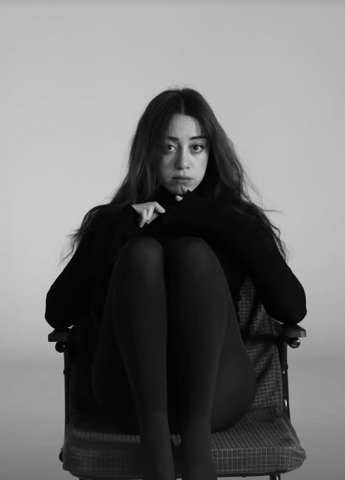Black and white editorial portrait of a woman curled up in black